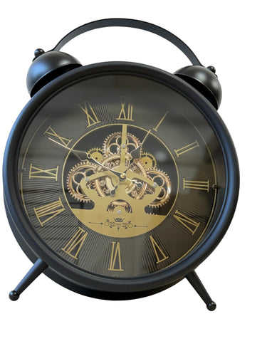 A black twin-bell alarm clock with a transparent glass face showing an ornate gold inner gear mechanism and gold Roman numerals.