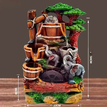 A decorative miniature water fountain sculpture with a rustic forest theme, featuring wooden buckets, flowing water, elephant figures, green foliage, and a reddish-brown trunk