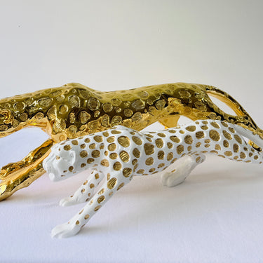 Gold prowling big cat sculpture beside a white version with gold spots
